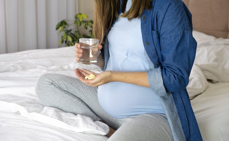 Pregnant woman hold pills for prenatal and glass of water.