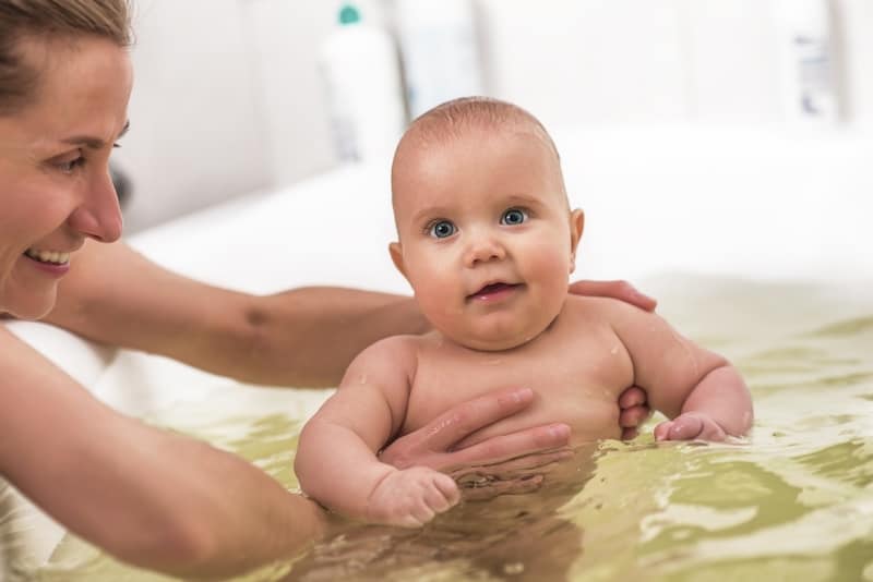 A woman is holding a newborn baby in a bathtub.