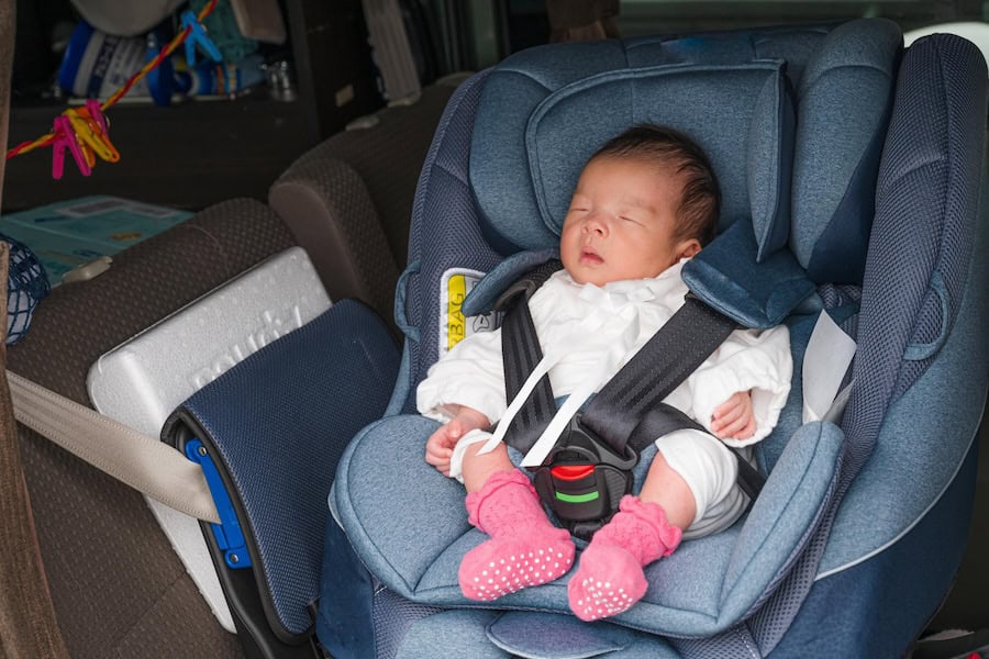 A baby sleeps peacefully in a blue car seat.