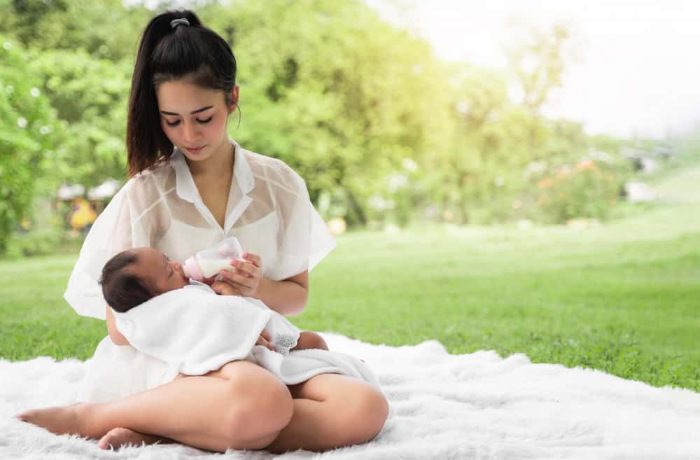 A mom feeding her baby with a bottle in grassy outdoors.