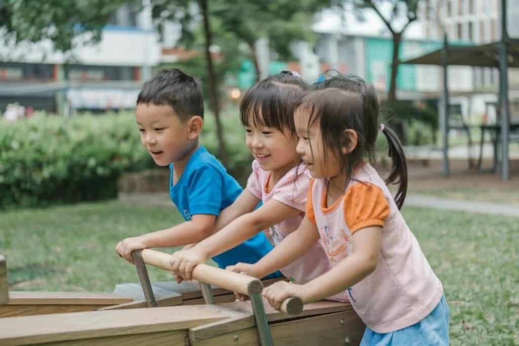 Three young children playing outdoors on wooden equipment